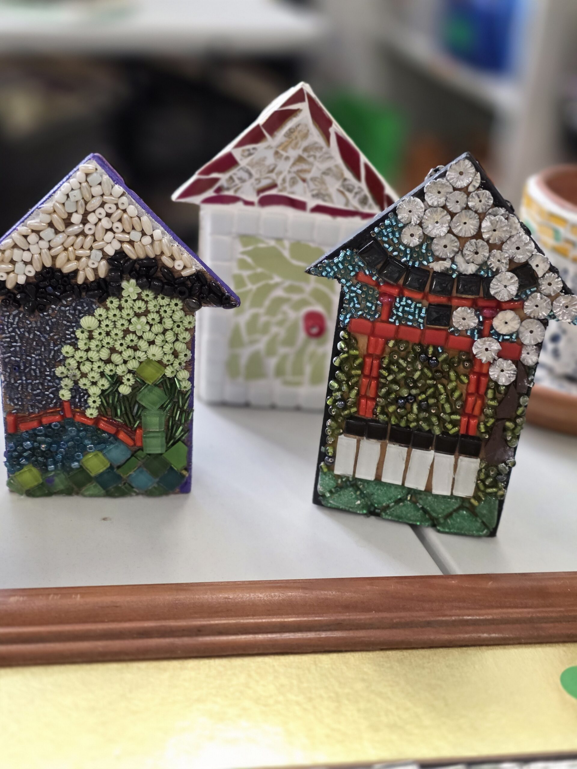 Three small handmade mosaic ceramic house sculptures displayed on a shelf.